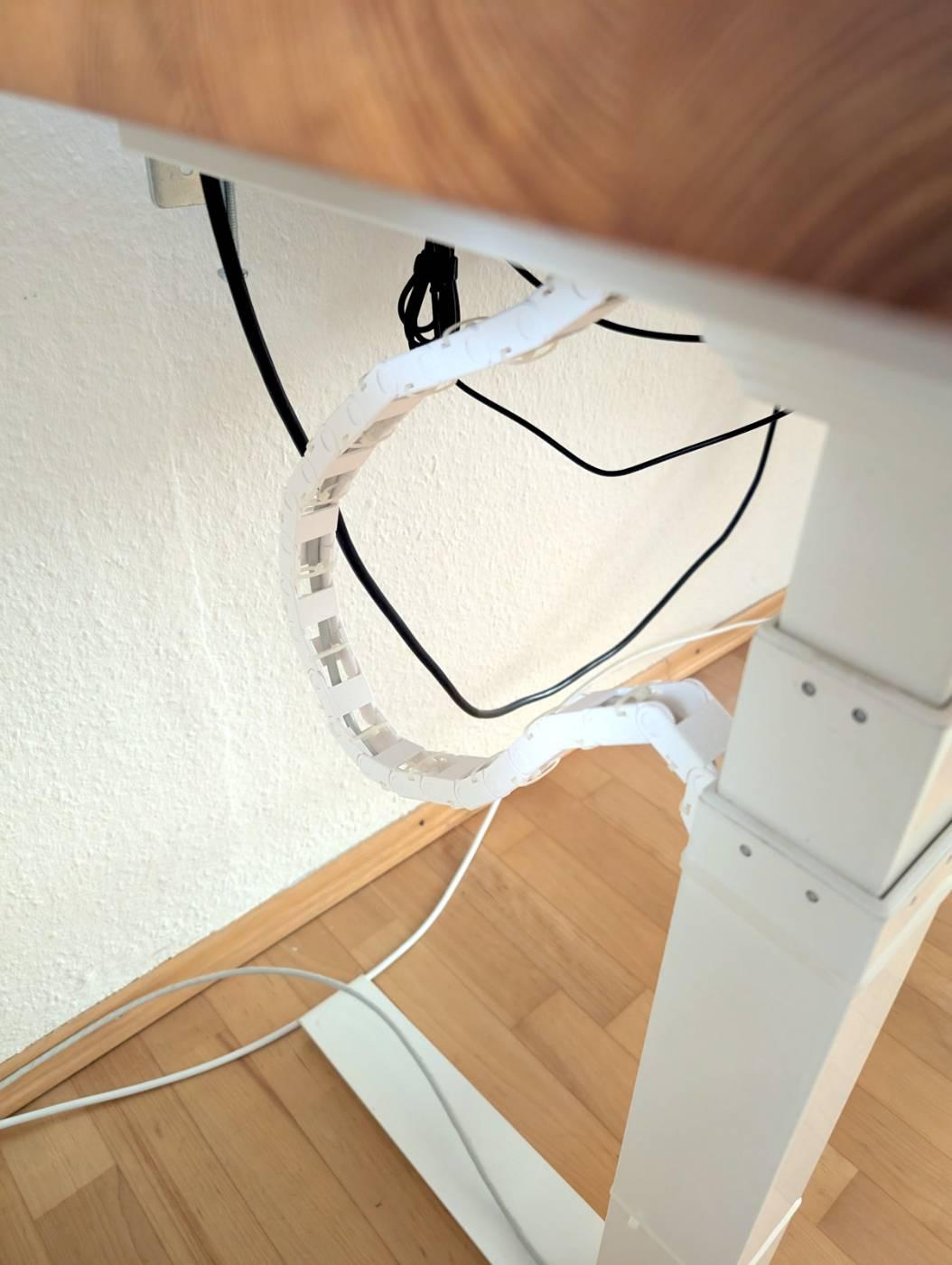 Photo of the side of a standing desk. It has white frame and a wooden desktop.

The desk is in a lower position and the 3D-printed cable chain creates a slack loop. The cable inside the chain is protected from tangling.