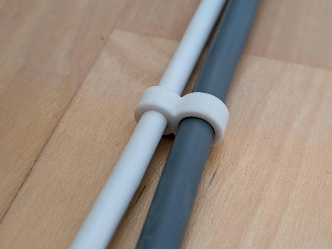 Photo of two cables on a wooden floor, one white, the other a dark shade of blue.

The cables are held together by a clip that looks like two fused rings with the diameters matching those of the cables.